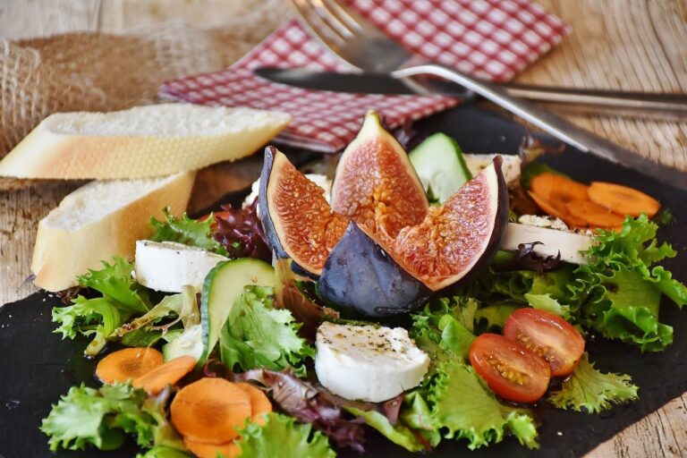 A beautifully plated and nutritional well-rounded fig and cheese surrounded by greens and other healthy foods and two slices of bread