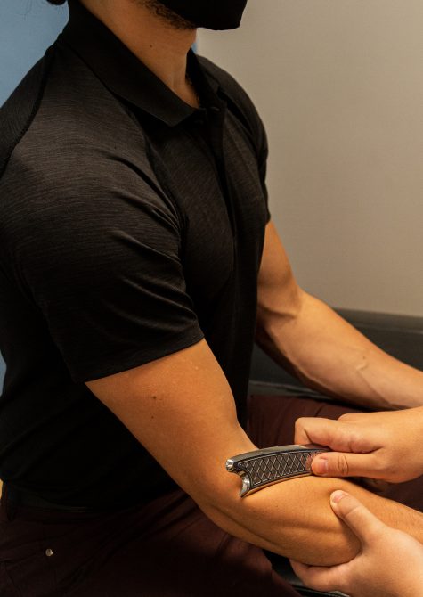 Sports chiropractor in bellingham performing muscle relaxation therapy using an instrument (known as IASTM) on the patients forearm in a way often used to treat tennis elbow, carpal tunnel, or golfers elbow.